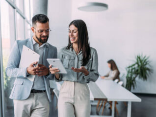 Shot of a two confident business persons talking in the work place. Two colleagues using a digital tablet while walking in a modern office. Businessman and businesswoman in meeting discussing business strategy. Business coworkers working together in the offic